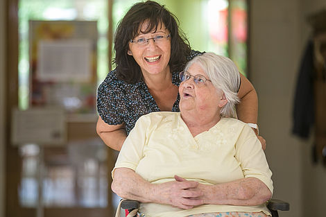 Von einer Pflegerin wird eine Seniorin im Rollstuhl geschoben. 