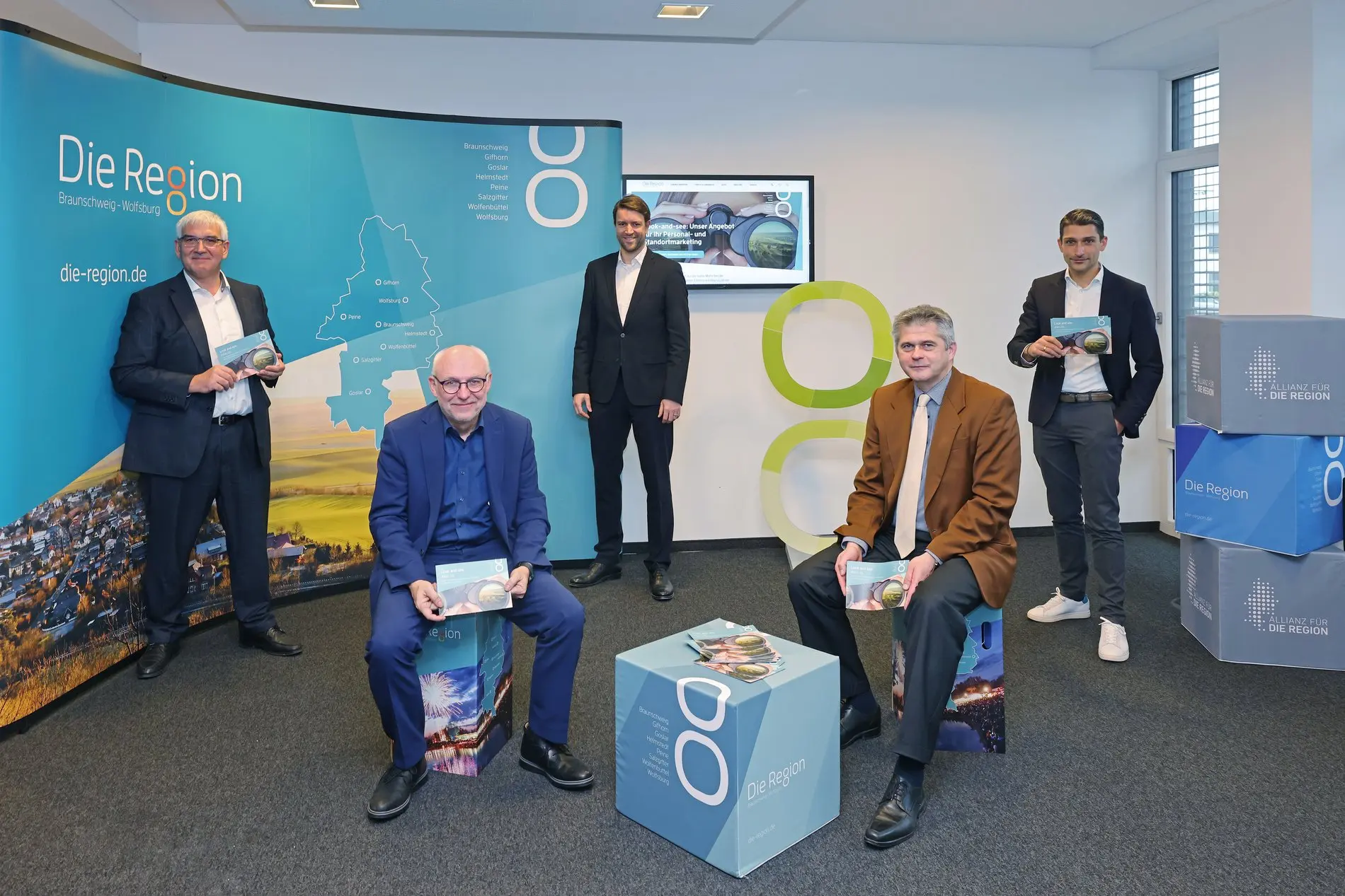 Fünf Männer stehen und sitzen, schauen in die Kamera und präsentieren einen Flyer der Allianz für die Region.