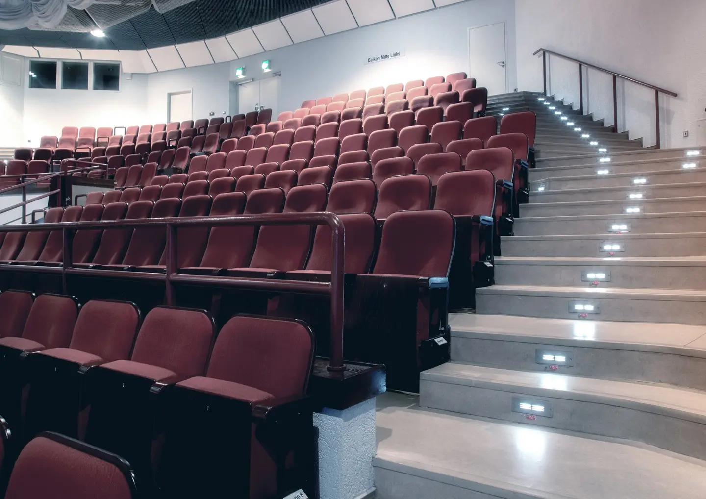 Der große, leere Saal des CongressPark Wolfsburg mit roten Klappsitzen, eine Treppe führt daran rechts vorbei nach oben.
