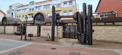 Man blcikt auf ein Gebäude mit Sandsteinfassade. Vor dem Gebäude stehen abstrakte Skulpturen.