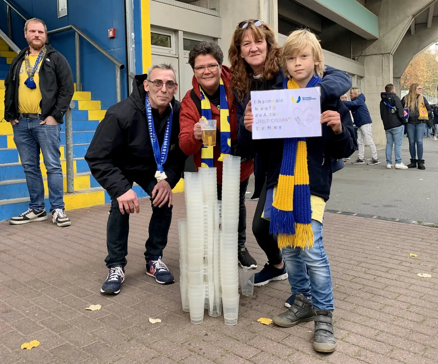 Ein Junge und drei Erwachsene vor dem Eintracht-Stadion. Der Junge hält ein Schild in die Kamera. 