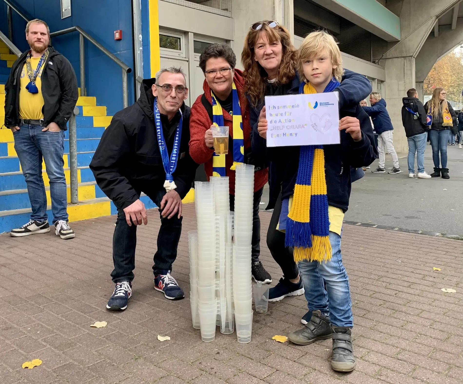 Ein Junge und drei Erwachsene vor dem Eintracht-Stadion. Der Junge hält ein Schild in die Kamera. 