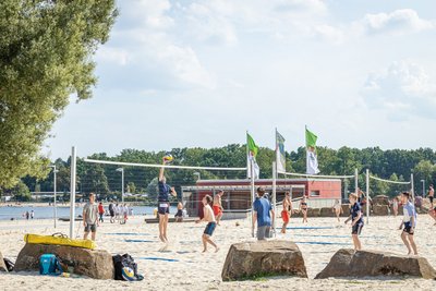 Man blickt auf eine Gruppe von Personen auf einem Beachvolleyballplatz an einem Strandabschnitt des Allersees