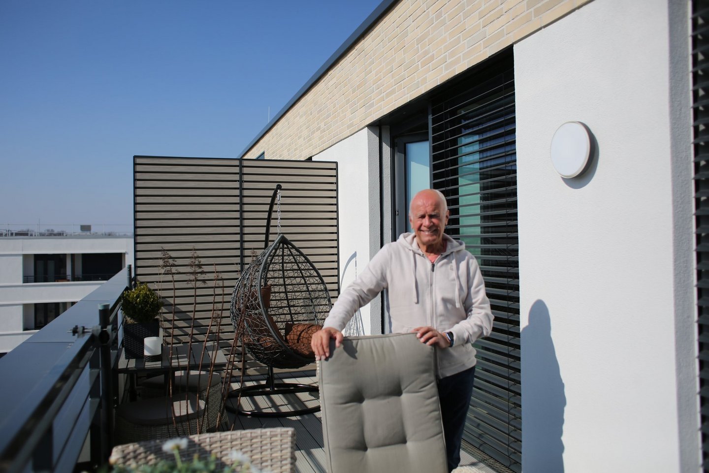 Ein Mann stützt sich auf einen Stuhl auf einer Dachterrasse.