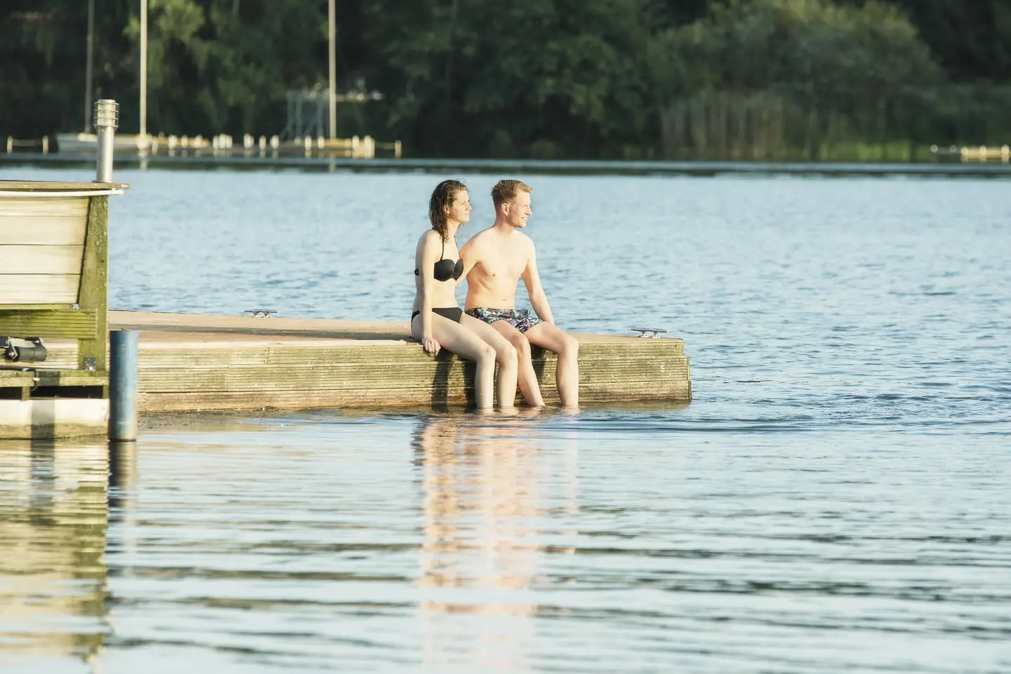 Zwei Badegäste sitzen auf dem Steg am Allersee in Wolfsburg.