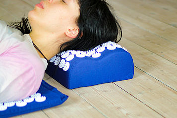 Eine junge Frau liegt mit dem Kopf auf einem Akkupunkturkissen.