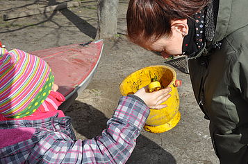 Ein Mädchen zeigt Mitarbeiterin Jennifer Polo einen gelben Eimer. 