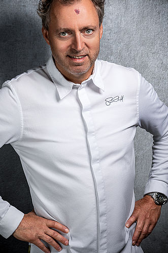 Ein Mann in weißem Koch-Outfit.