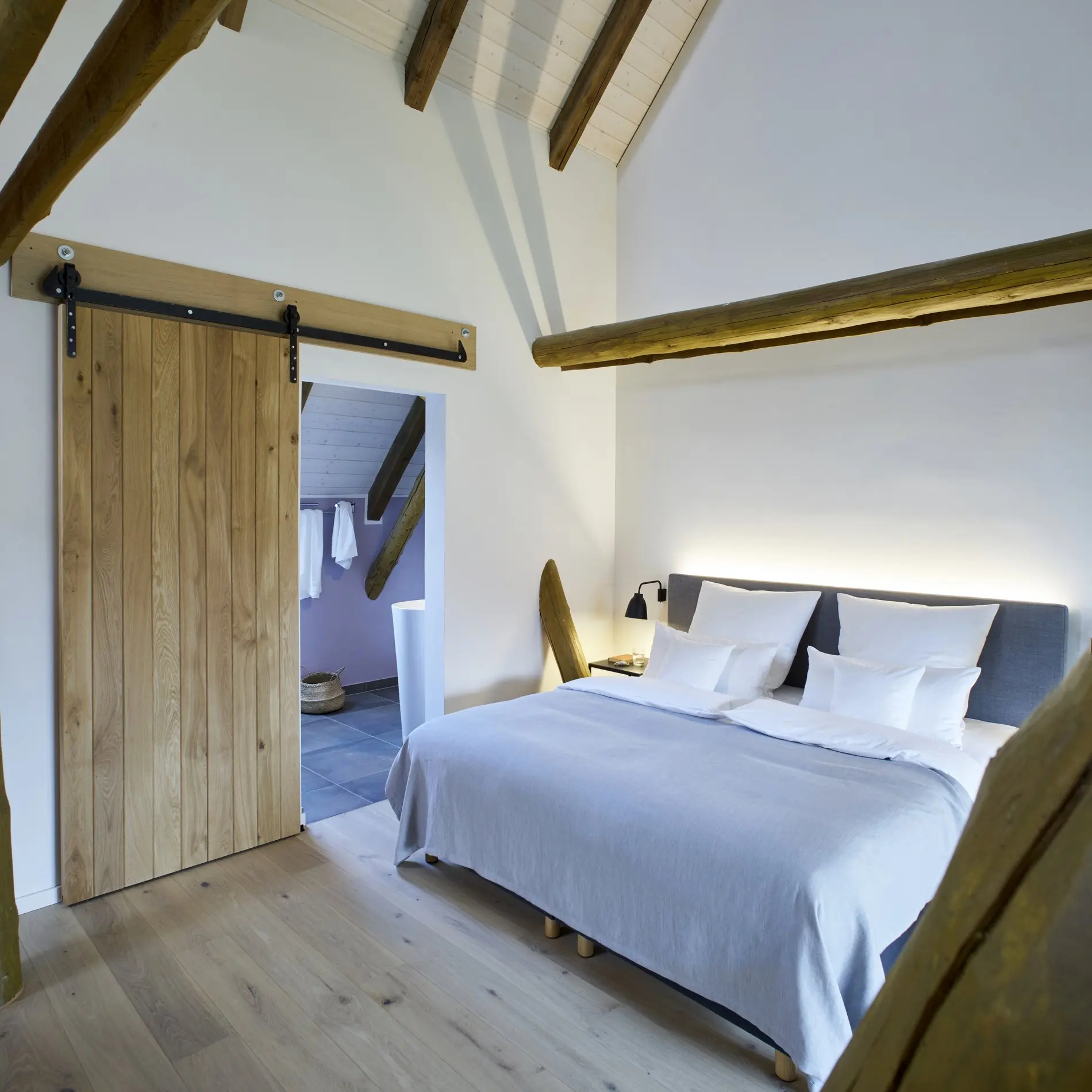 Ein Zimmer in einem Boarding House in Wolfsburg. Die Wände sind weiß gestrichen, die Türen, der Fußboden und die offenliegenden Dachstreben sind aus Holz.