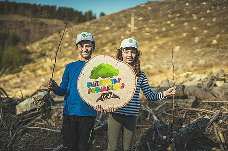 Zwei Kinder halten Baum-Setzlinge und eine UKF-Baumscheibe in den Händen.