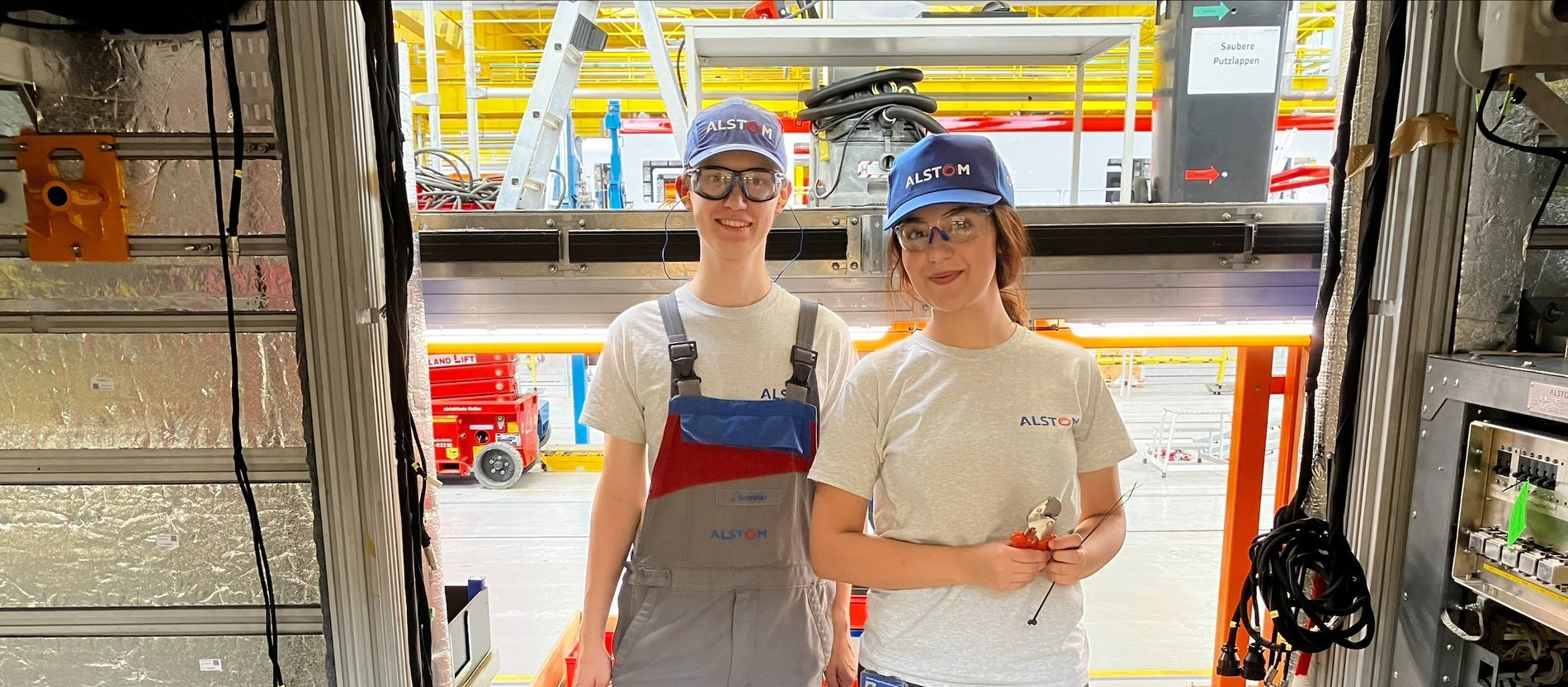Zwei junge Auszubildende stehen im Türrahmen eines noch nicht fertigen Zuges in der Werkhalle von Alstom.