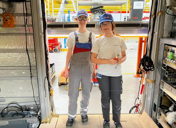 Zwei junge Auszubildende stehen im Türrahmen eines noch nicht fertigen Zuges in der Werkhalle von Alstom.