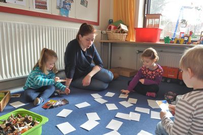 Frieda, Jennifer Polo und Leonie spielen auf einem blauen Teppich ein Memory-Spiel.