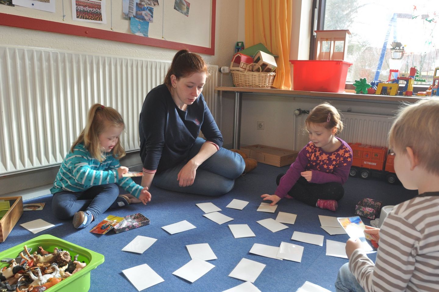 Frieda, Jennifer Polo und Leonie spielen auf einem blauen Teppich ein Memory-Spiel.