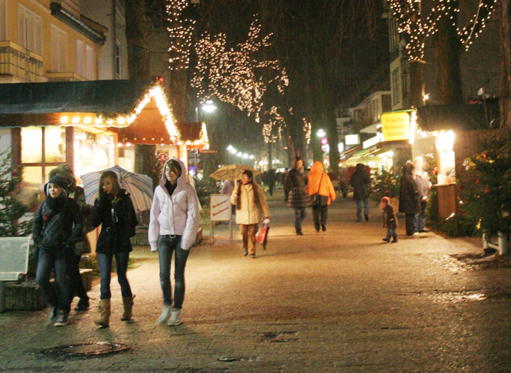 Eine abendliche  Fußgängerzone mit Fußgängern, dazu beleuchtete Buden.