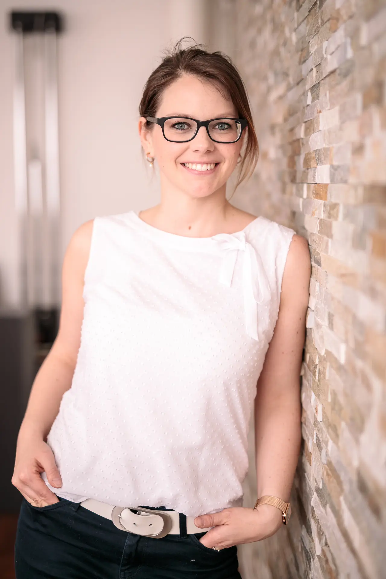 Eine junge Frau lehnt an der Wand und lächelt in die Kamera.