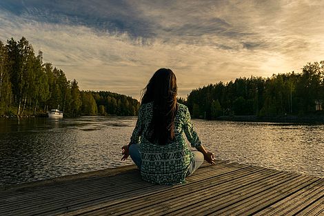 Eine Frau sitzt auf dem Steg vor einem See.