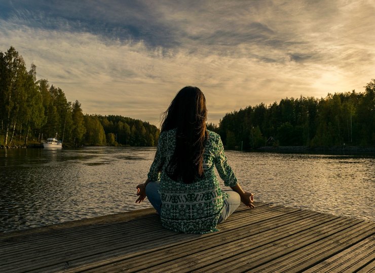 Eine Frau sitzt auf dem Steg vor einem See.
