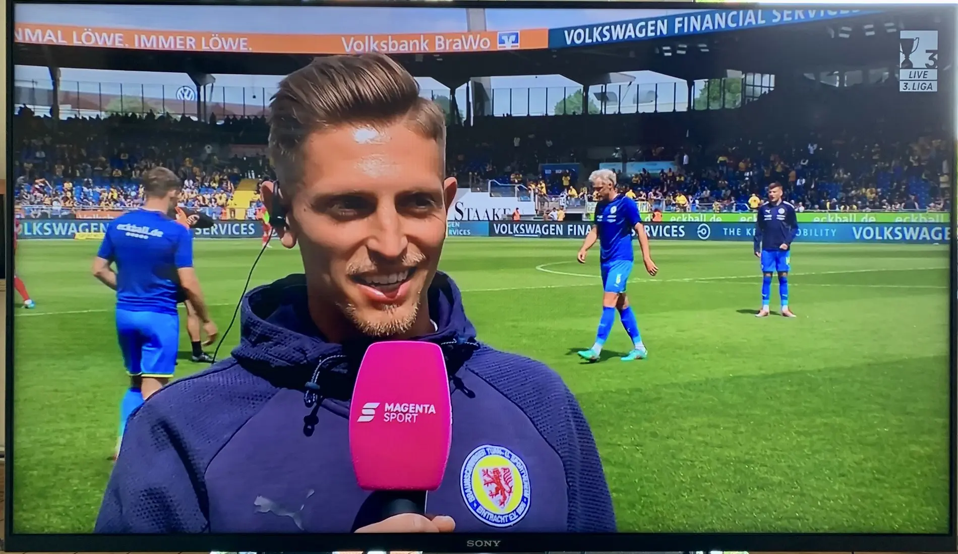 Ein Mann in einer Vereinsjacke gibt ein Interview.