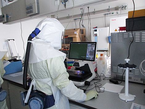 Eine Person in weißer Schutzkleidung steht an einem Labortisch.