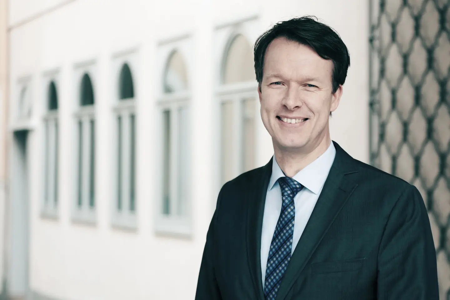 Ein Mann in dunkelblauem Anzug vor grauem Hintergrund.