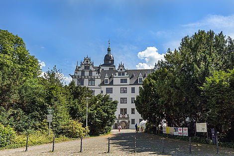 Ein historisches Schloss mit weißen Wänden und grauen Schiefer-Dachschindeln.