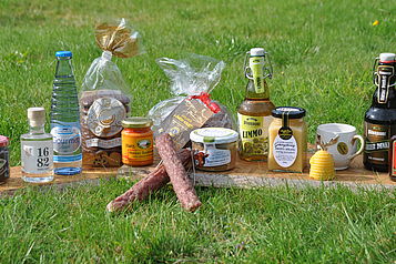 Verschiedene Harzer Produkte, etwa Honig und Bier, stehen auf einem Brett auf einer grünen Wiese.