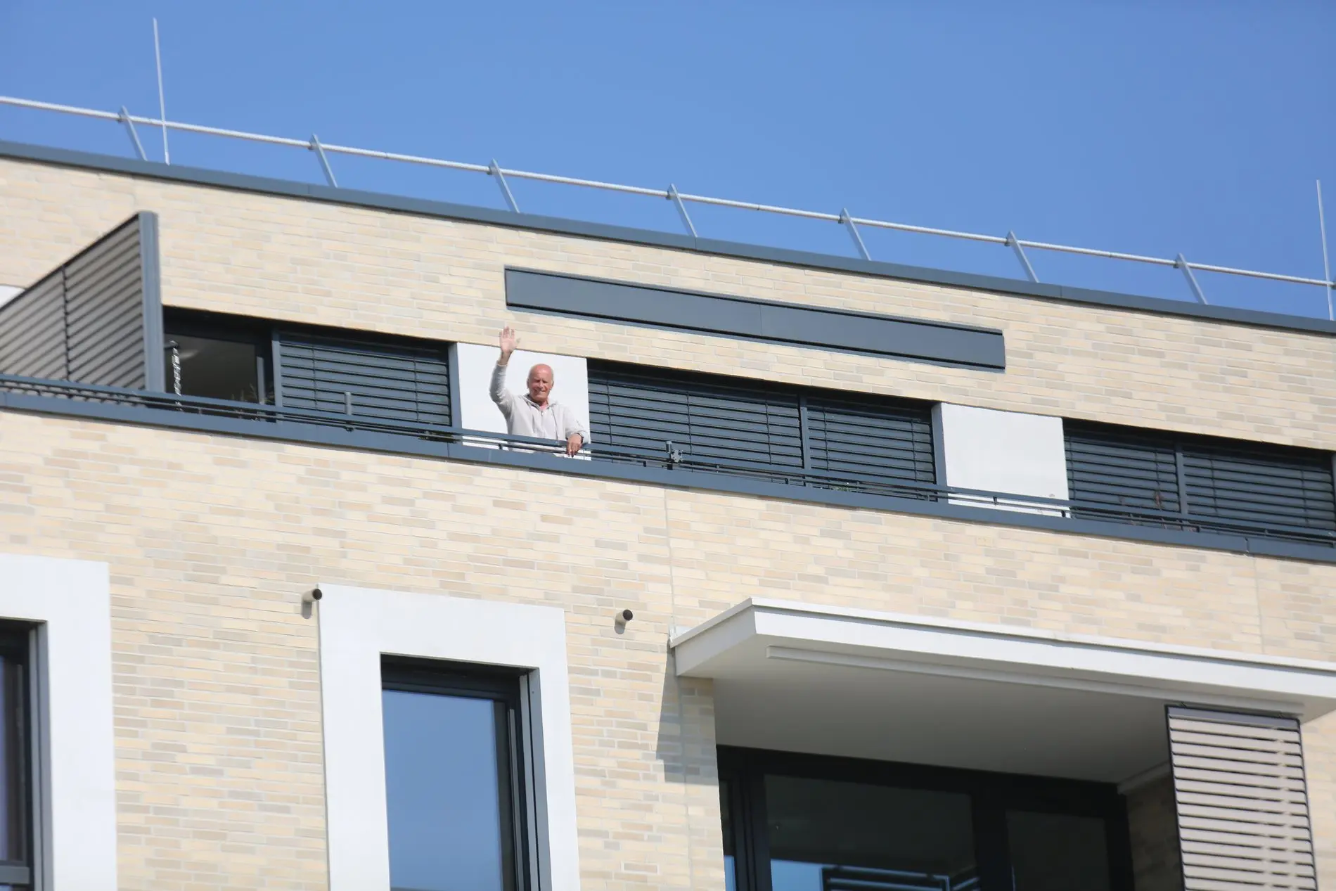 Ein Mann winkt von einer Dachterrasse herunter.