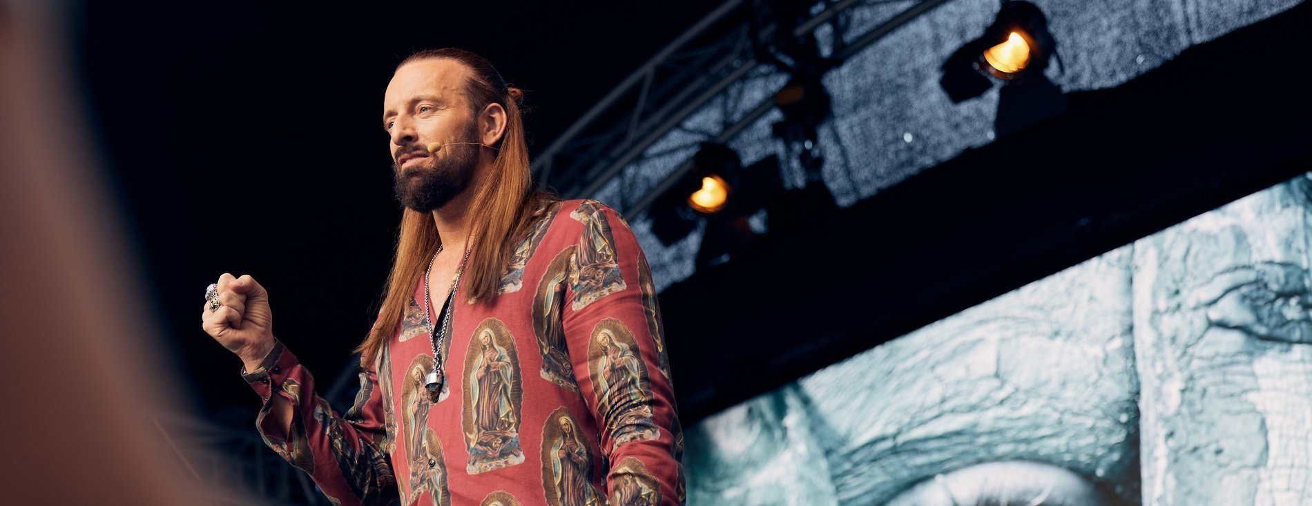 Ein langhaariger Mann spricht auf der Bühne.