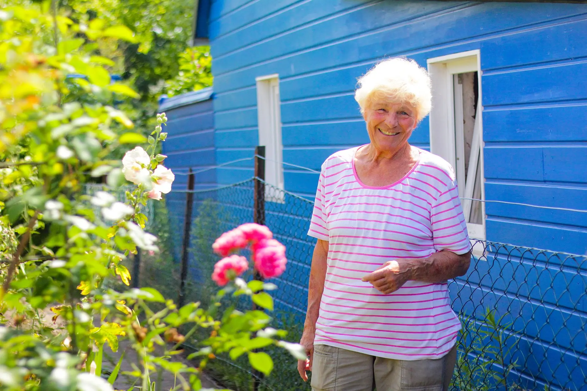 Eine Frau steht vor ihrem blauen Häuschen im Schrebergarten.