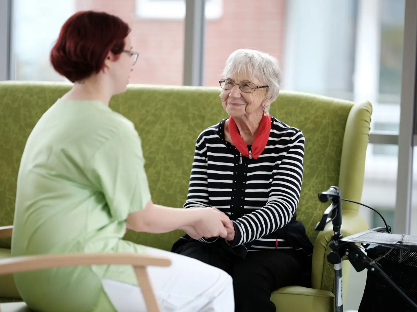 In einer Einrichtung hält eine Pflegerin die Hand einer Seniorin.