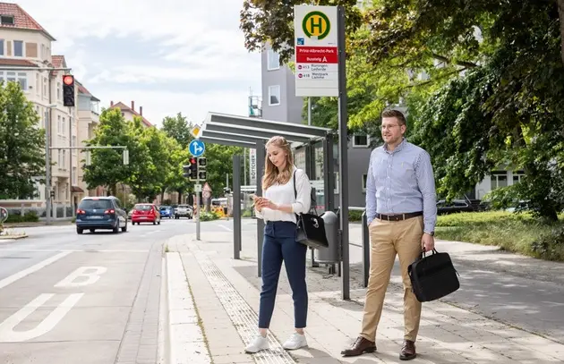 Eine Frau und ein Mann warten an einer Bushaltestelle.