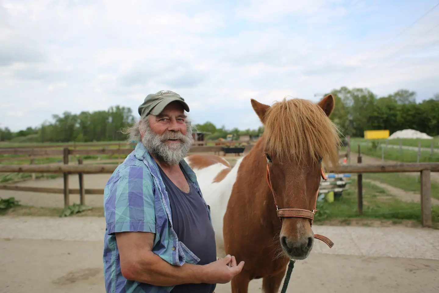 Ein Mann mit einem dichten Rauschebart steht neben einem Pferd, das er am Geschirr hält.