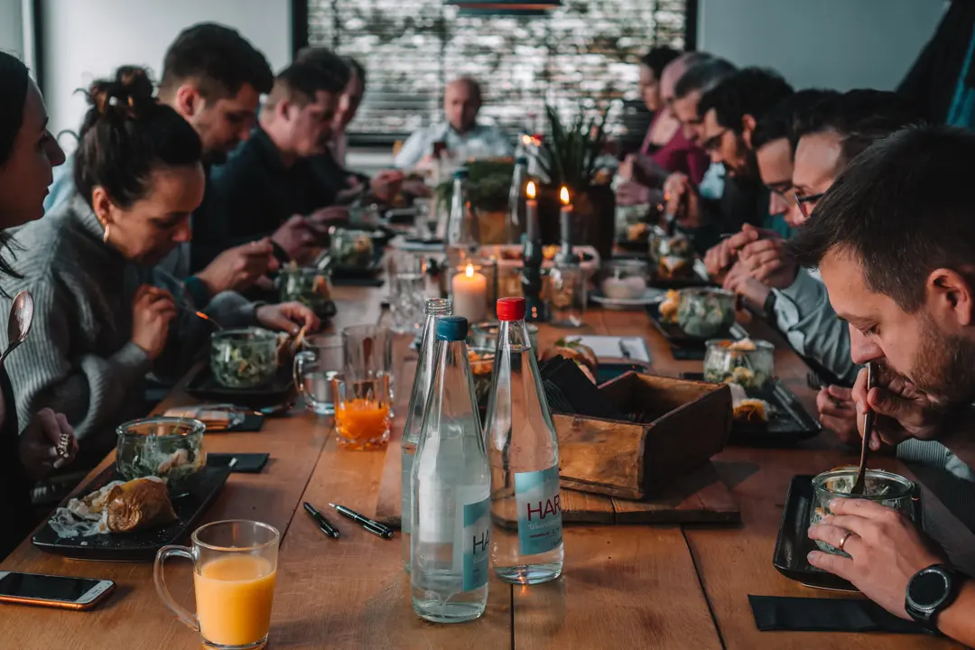 Menschen essen gemeinsam an einer langen Holztafel.