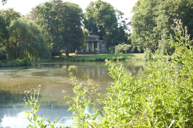 Ein Teich mit Baumbewuchs, im Hintergrund ein tempelartiges Gebäude.