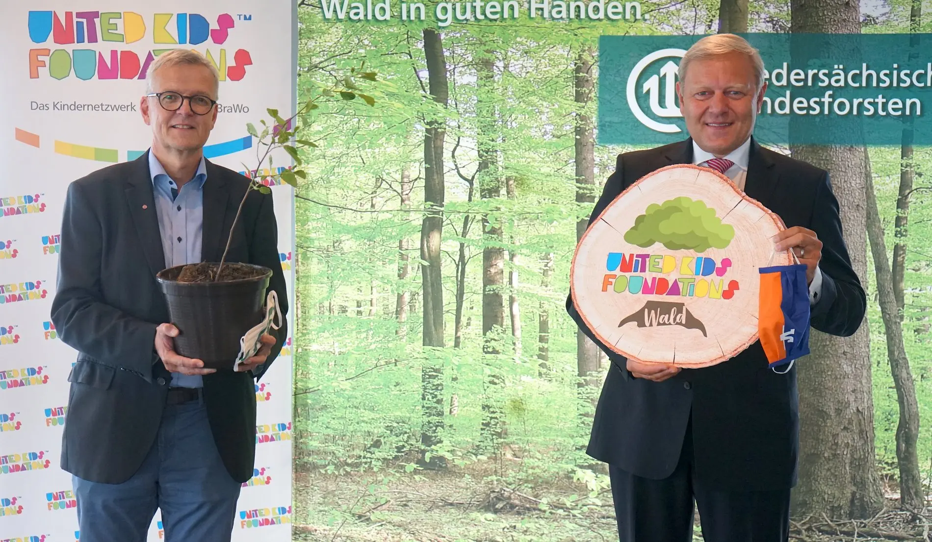 Dr. Klaus Merker und Jürgen Brinkmann vor einer Leinwand mit Wald und dem Logo der United Kids Foundation.