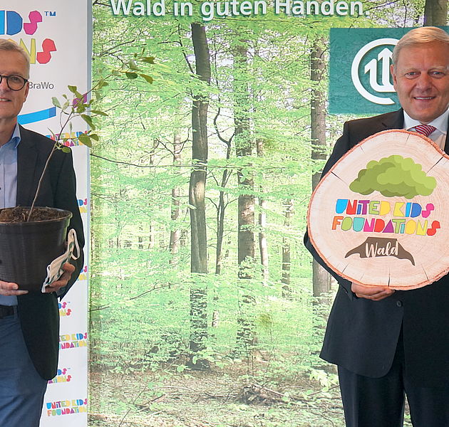 Dr. Klaus Merker und Jürgen Brinkmann vor einer Leinwand mit Wald und dem Logo der United Kids Foundation. (Bildrechte: Beate Ziehres)