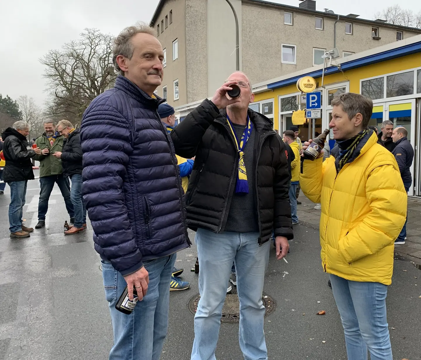Drei Personen stehen vor einem Stadion.