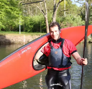 Ein Kanut steht an einem Fluss. Über seine rechte Schulter hat er ein Kanu gelegt, in der rechten Hand hält er ein Paddel. (Bildrechte: Frank Spyra)