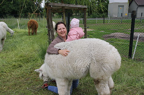 Eine Frau hält ein Kind auf dem Arm und streichelt ein Alpaka.
