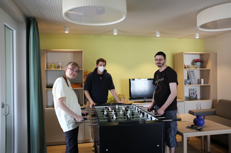 Zwei Männer und eine Frau stehen an einem Kickertisch.