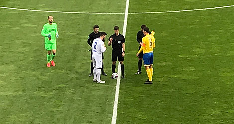 Zwei Fußballer mit Schiedsrichtern im Mittelkreis.