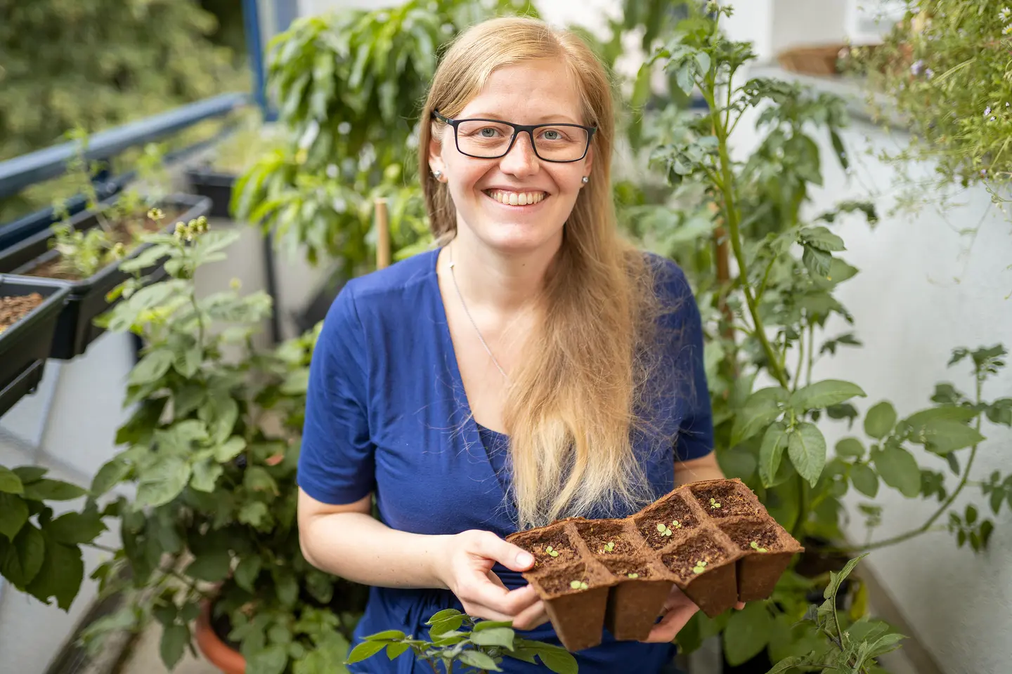 Eine junge Frau auf dem Balkon hält eine Box mit Pflanzenschösslingen