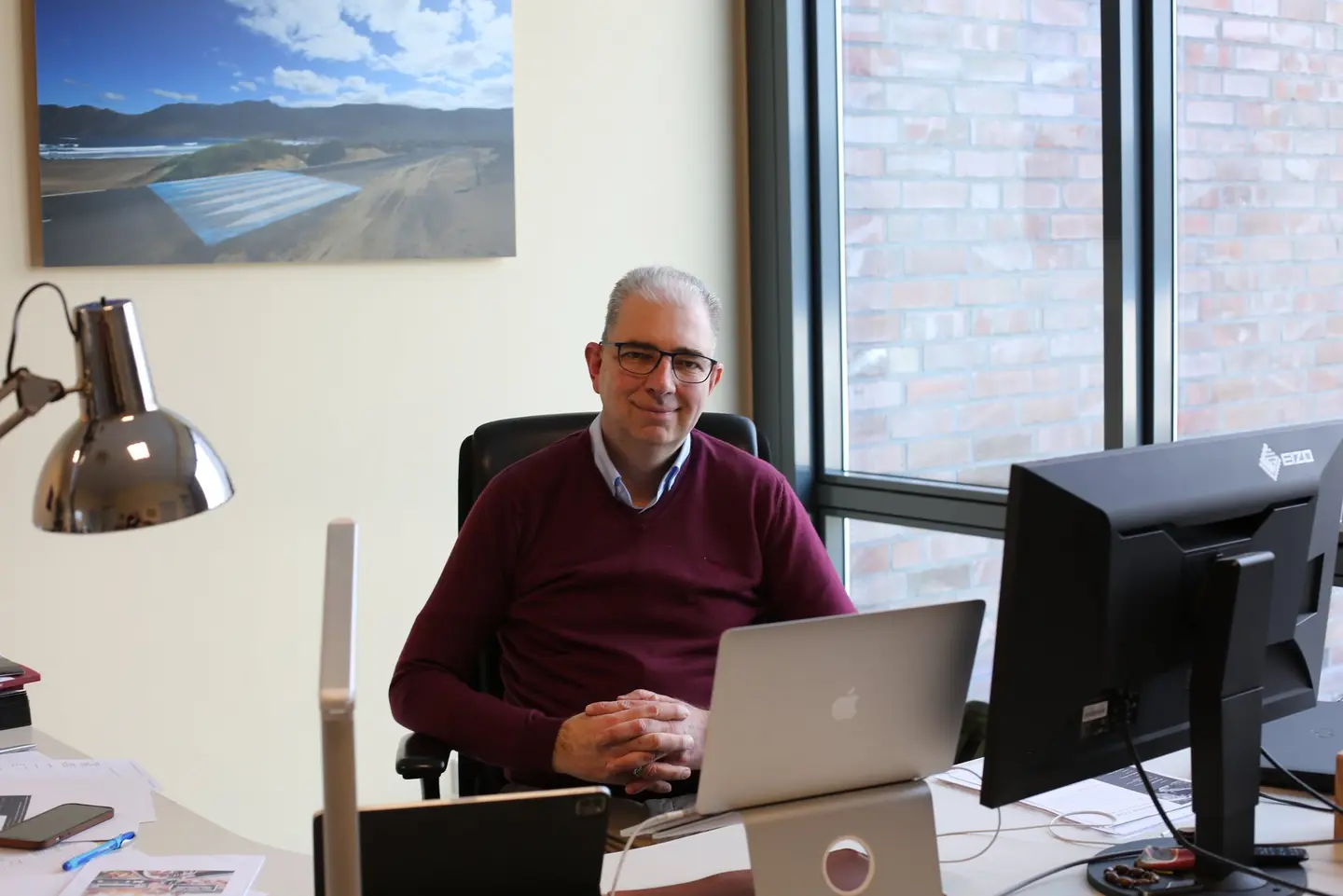 Ein Mann in rotem Pullover sitzt an einem Schreibtisch.