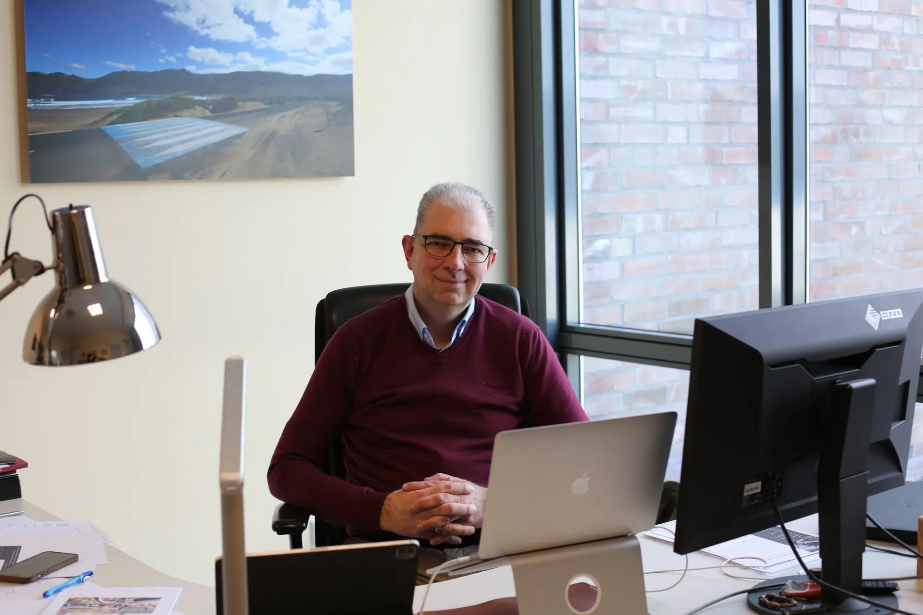 Ein Mann in rotem Pullover sitzt an einem Schreibtisch.