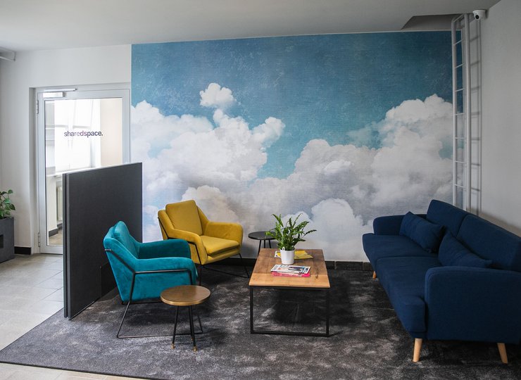 Verschiedenfarbige Sofas vor einer Wand mit Wolkenmotiv.