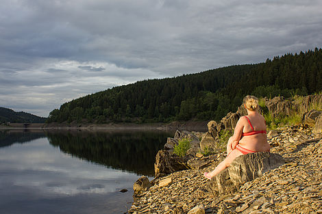 Ein Badegast sitzt am steinigen Ufer des Okerstausees.