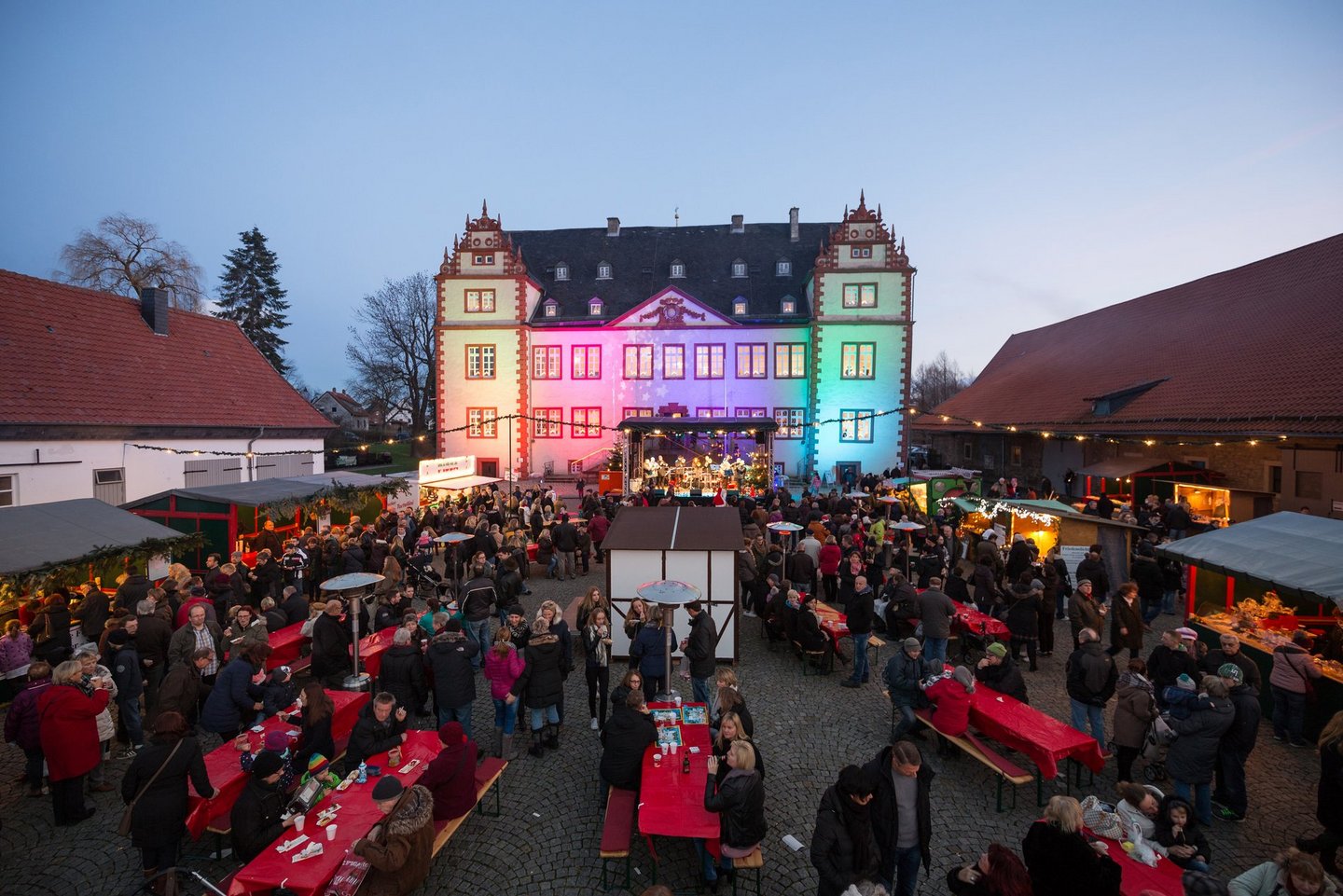 Man blickt aus der Vogelperspektive auf den gut besuchten Innenhof des Schlosses in Salder. Im Hintergrund ist das Schloss Salder bunt beleuchtet.