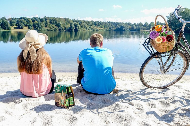 Eine Frau und ein Mann sitzen mit einem Fahrrad am See.