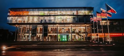 Ein erleuchtetes, modernes Gebäude mit Glasfront, davor einige Flaggen.